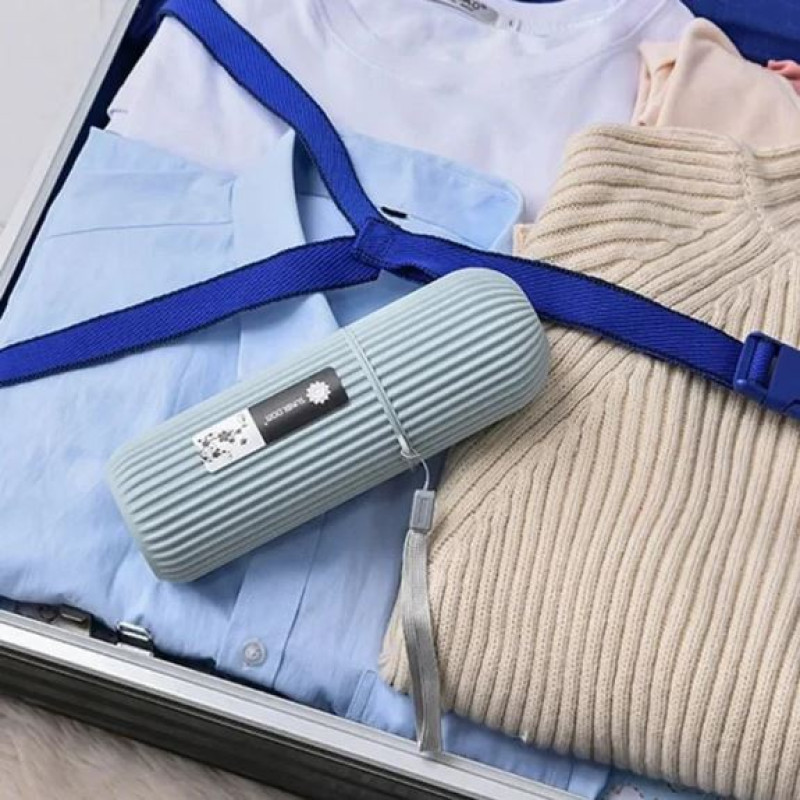 A grey toothpaste case organizer placed neatly inside a suitcase on top of folded clothes, showing its compact size for travel.